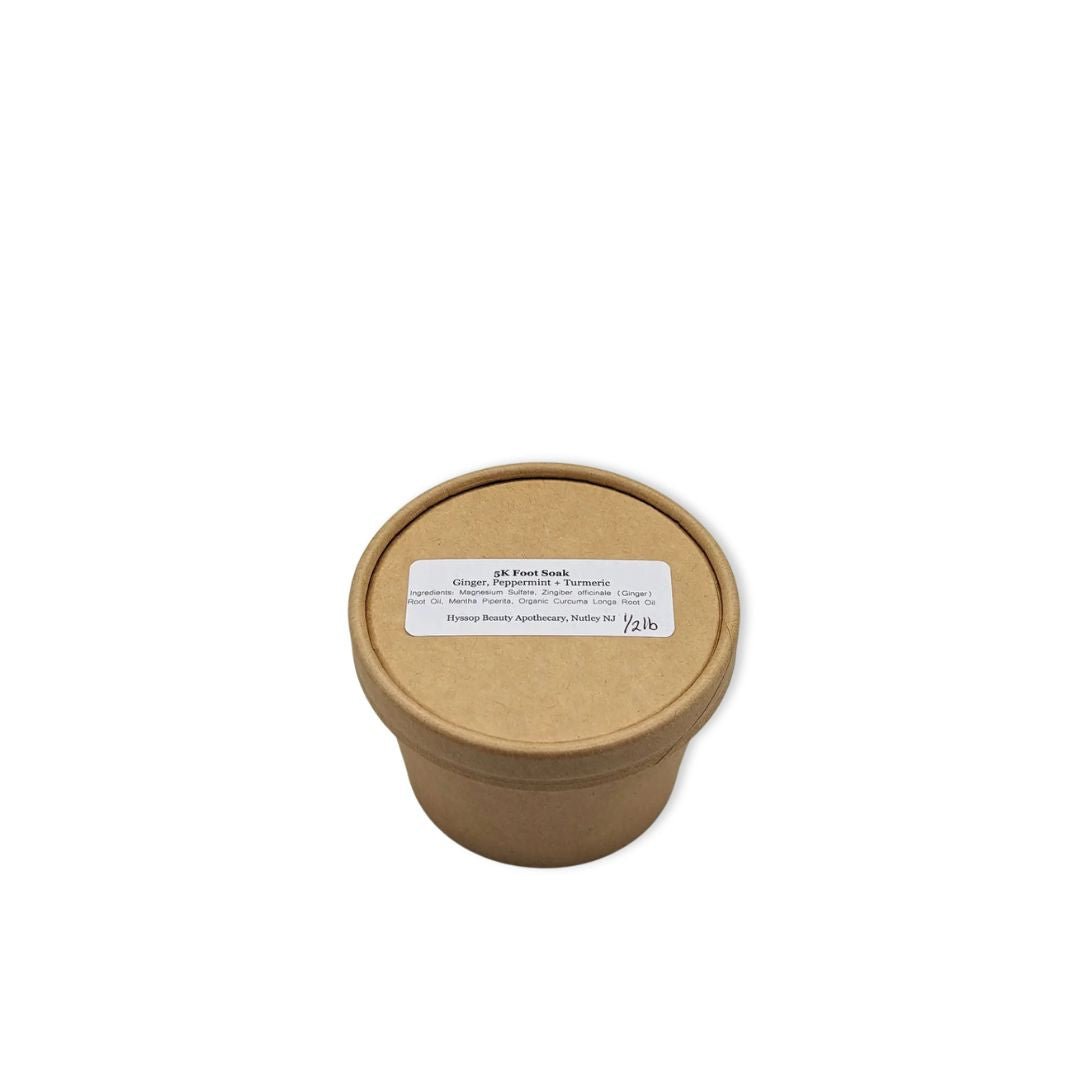 Cardboard cup of magnesium foot soak infused with turmeric + ginger with a label on a white background