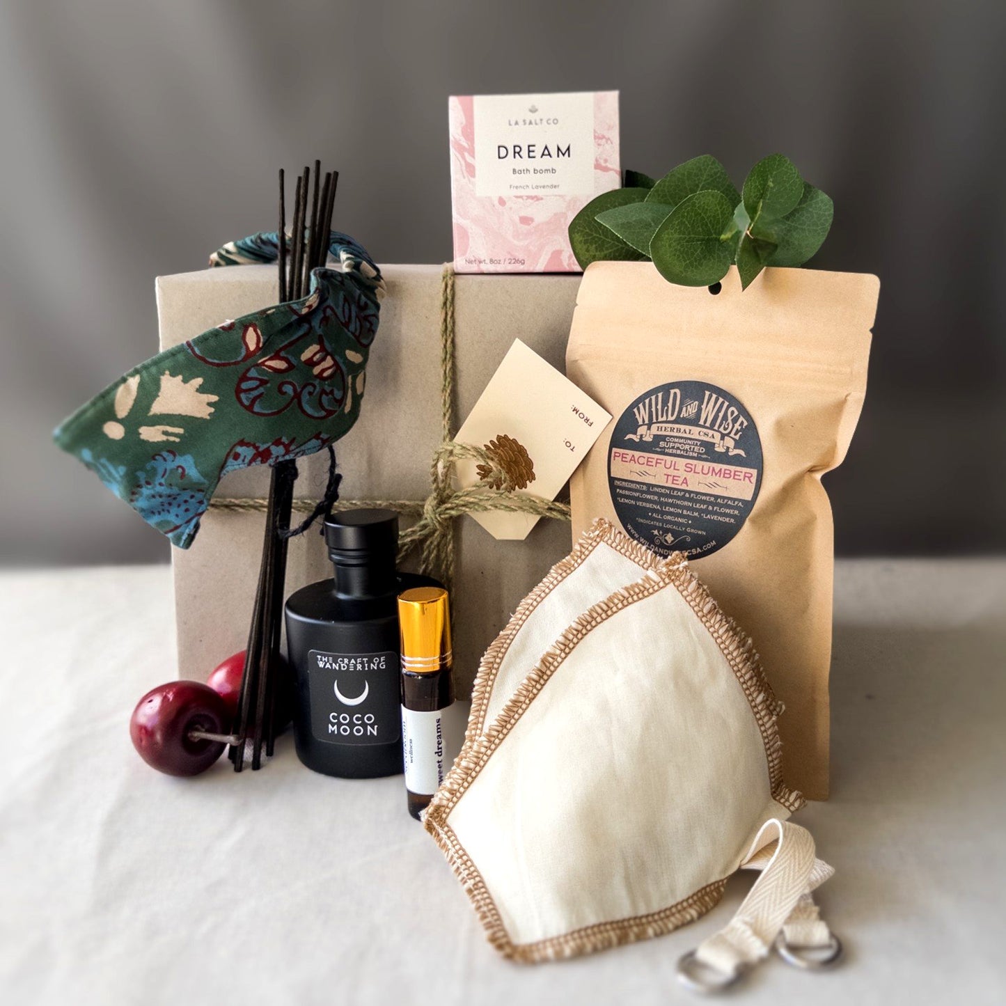 Items from the Sweet Slumber Natural Sleep kit including bath bomb, eye mask, aromatherapy, and tea in front of a wrapped gift box.