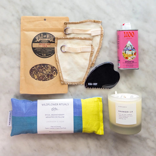 Stress relief care package contents with candle, eye pillow, tea, gua sha and body oil.