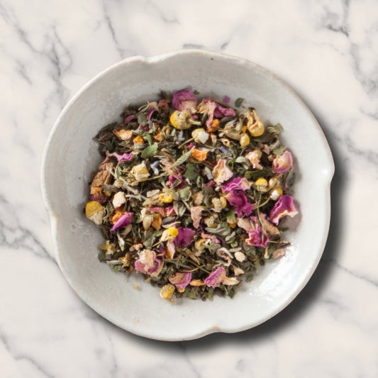 A top-down view of the Dream Catcher Organic Herbal Tea in a white bowl as a loose leaf mix of dried herbs and flowers .