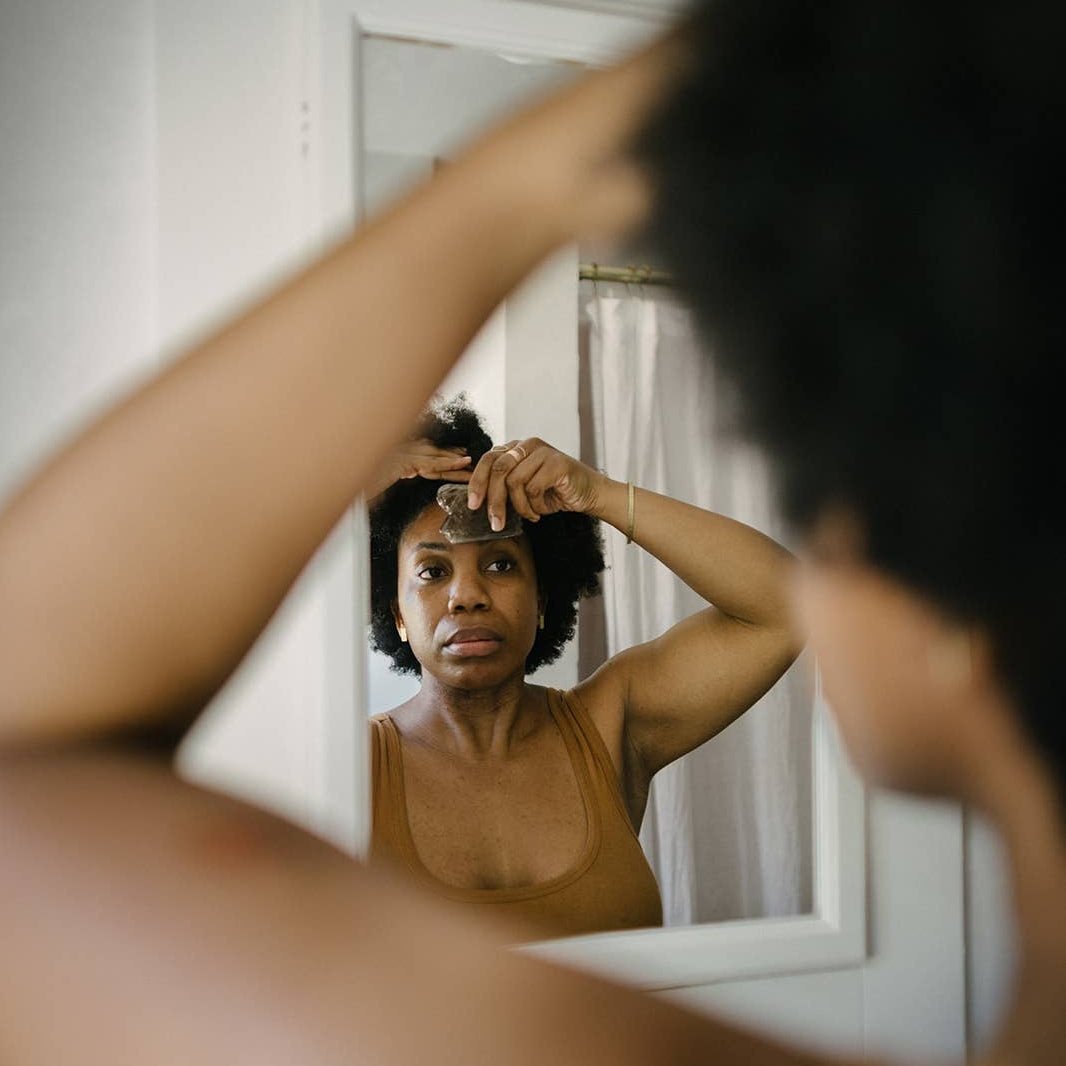 A woman looking in the mirror while using a Gua Sha tool