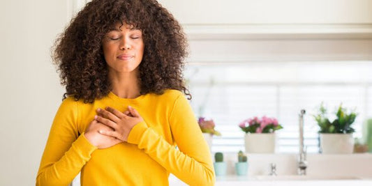 A woman in a yellow sweater with her eyes closed and her hands over her heart