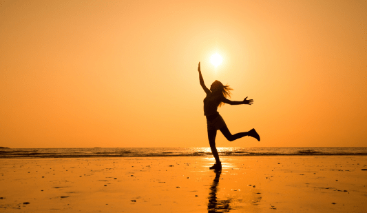 Woman dancing on a beach with a setting sun behind her