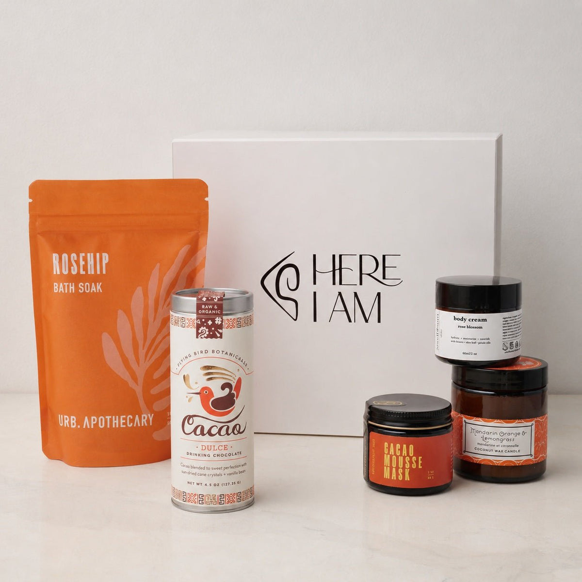 A blissful bath starts with the Bliss box shown here with a Cacao mask, mandarin orange lemongrass candle, rose blossom hand lotion, cacao dulce for drinking, and the rosehip bath soak from URB Apothecary with the Here I Am gift box in the background.