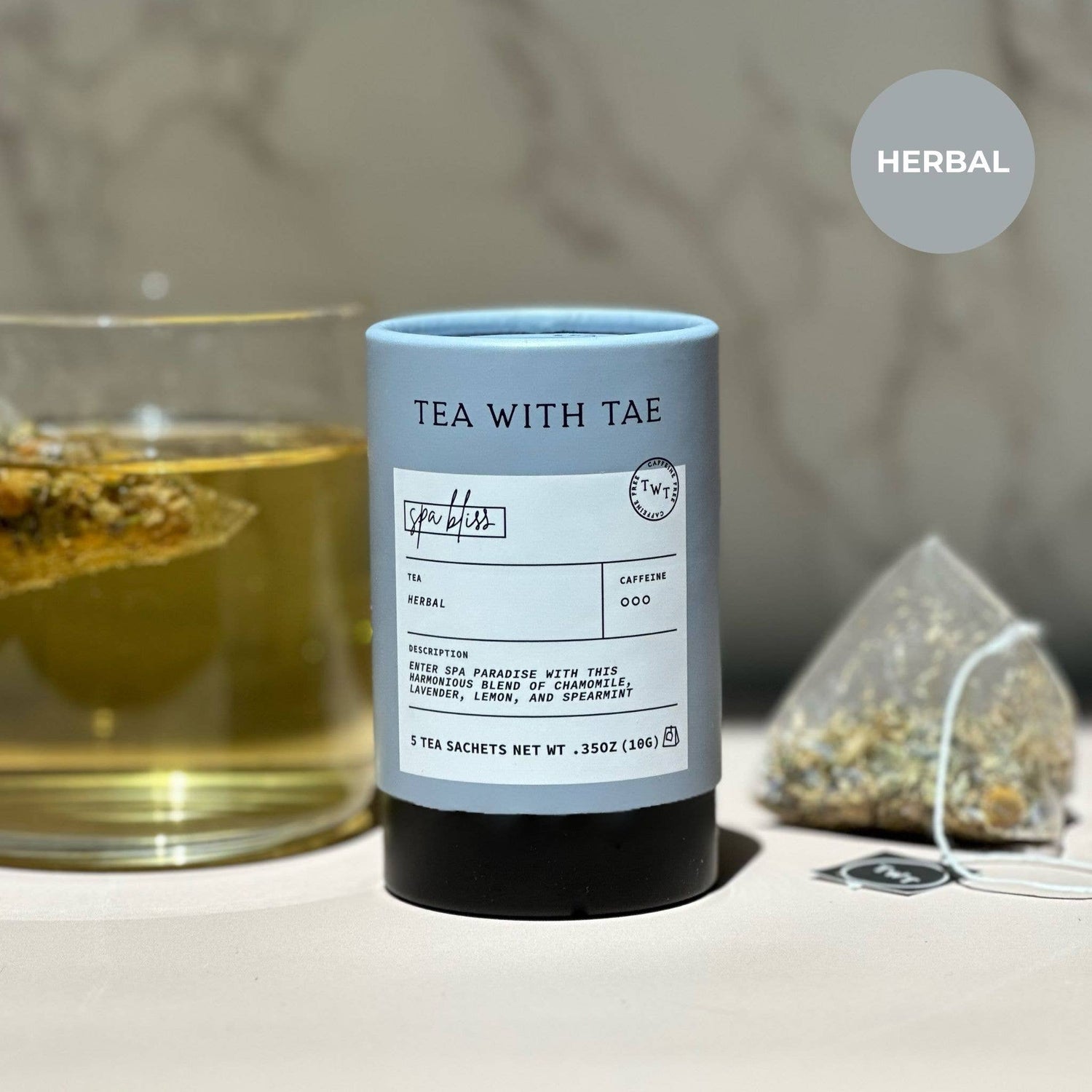 Spa Bliss Tea packaging with a glass of tea and loose tea leaves on a blurred background