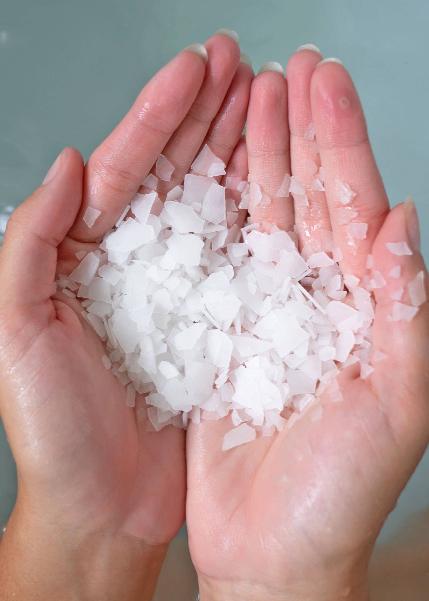 Two hands holding bath flakes against a neutral background. 