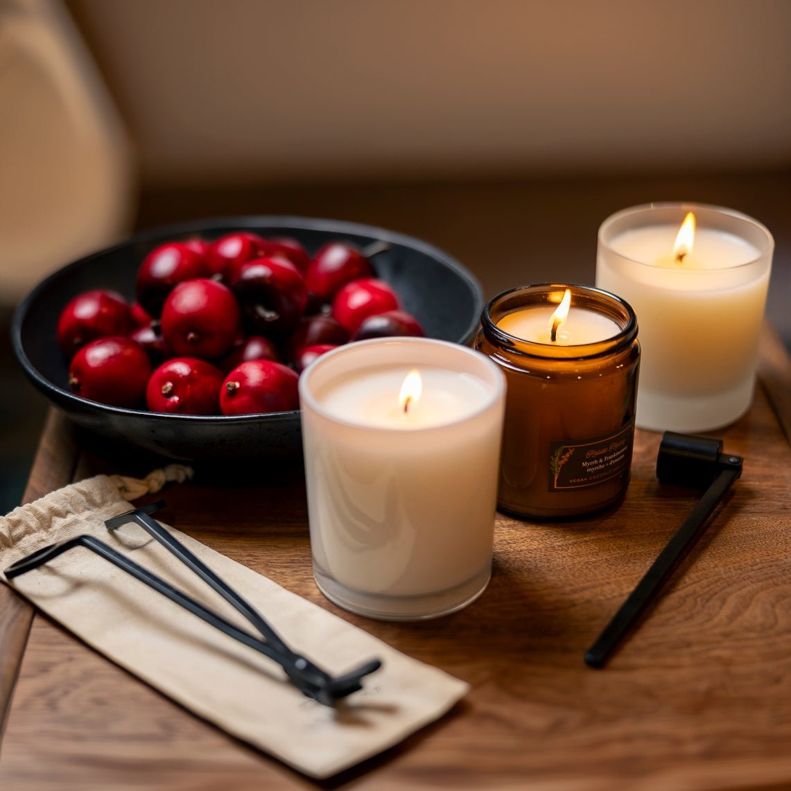 Three candles with wick trimmer and snuffer near a bowl with red apples