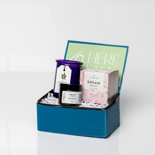 Blue box with Dream Bath Bomb, French Lavender Candle, and Rose Blossom Lotion on white background.