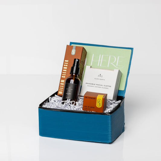 Blue gift box containing Pot of Gold Regenerative Face Balm, Pro-Age Toner, Reusable Facial Cloths, and Willow Cleanser on white background