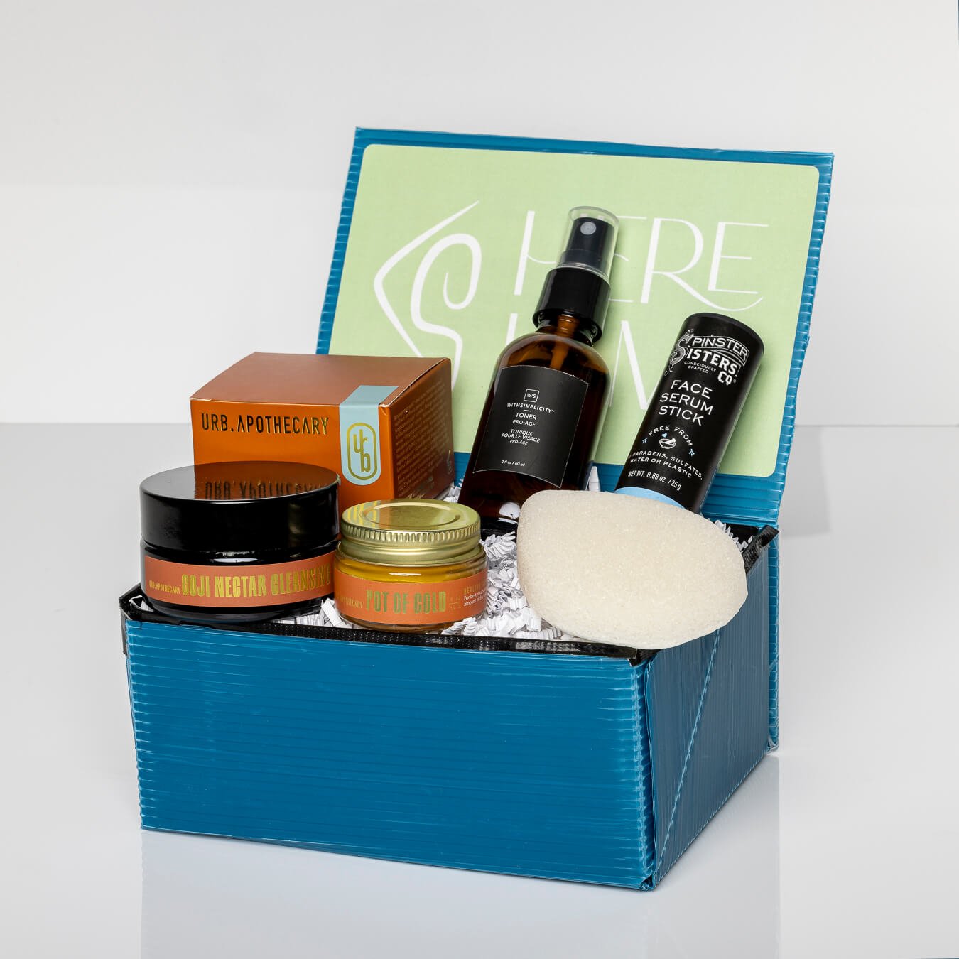 Blue gift box containing Pot of Gold Regenerative Face Balm, Pro-Age Toner, Konjac sponge, and Goji Nectar Cleanser, and Face Serum stick 