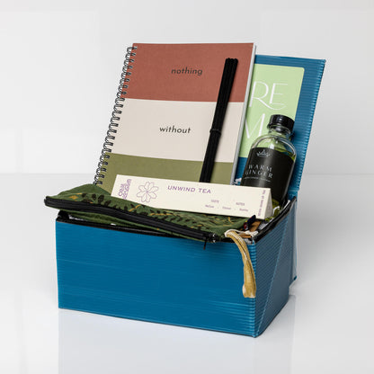 Blue gift box with an Intention Journal, pencil holder, Unwind Tea, and Warm Ginger Reed Diffuser.