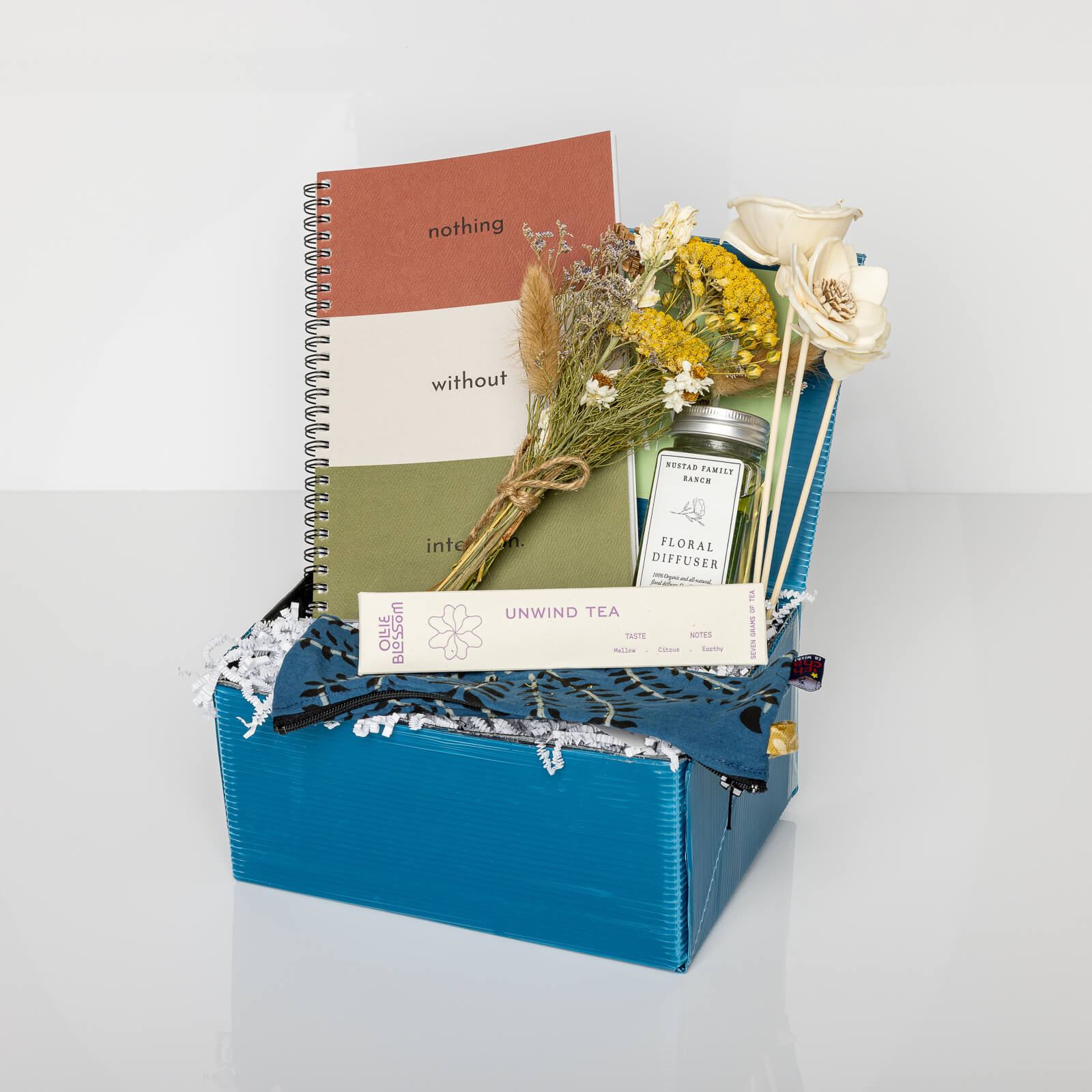 Blue gift box with an Intention Journal, pencil holder, Unwind Tea, and Reed Diffuser with dried flowers