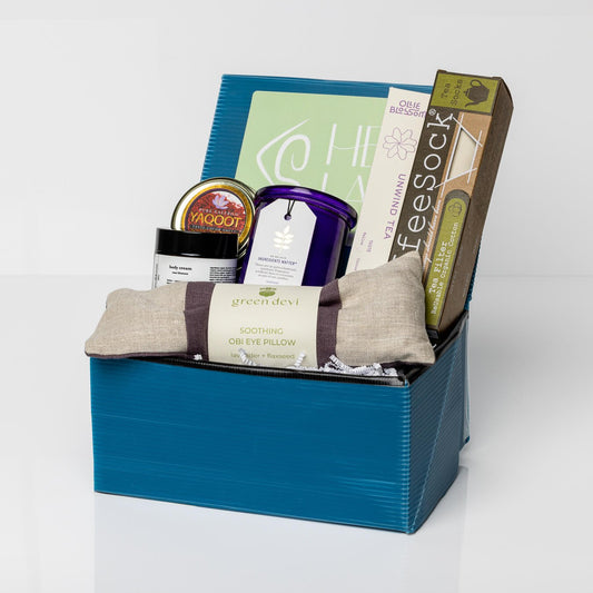 Blue box with French lavender aromatherapy candle, linen lavender eye pillow, saffron, reusable tea filters, rose hand lotion, and Unwind Tea.