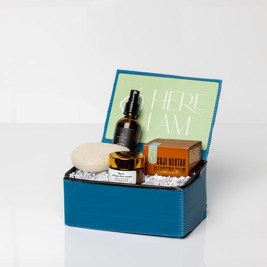 Blue skincare box with collagen face cream, goji nectar cleansing balm, konjac facial sponge, and pro-age toner on a white background.