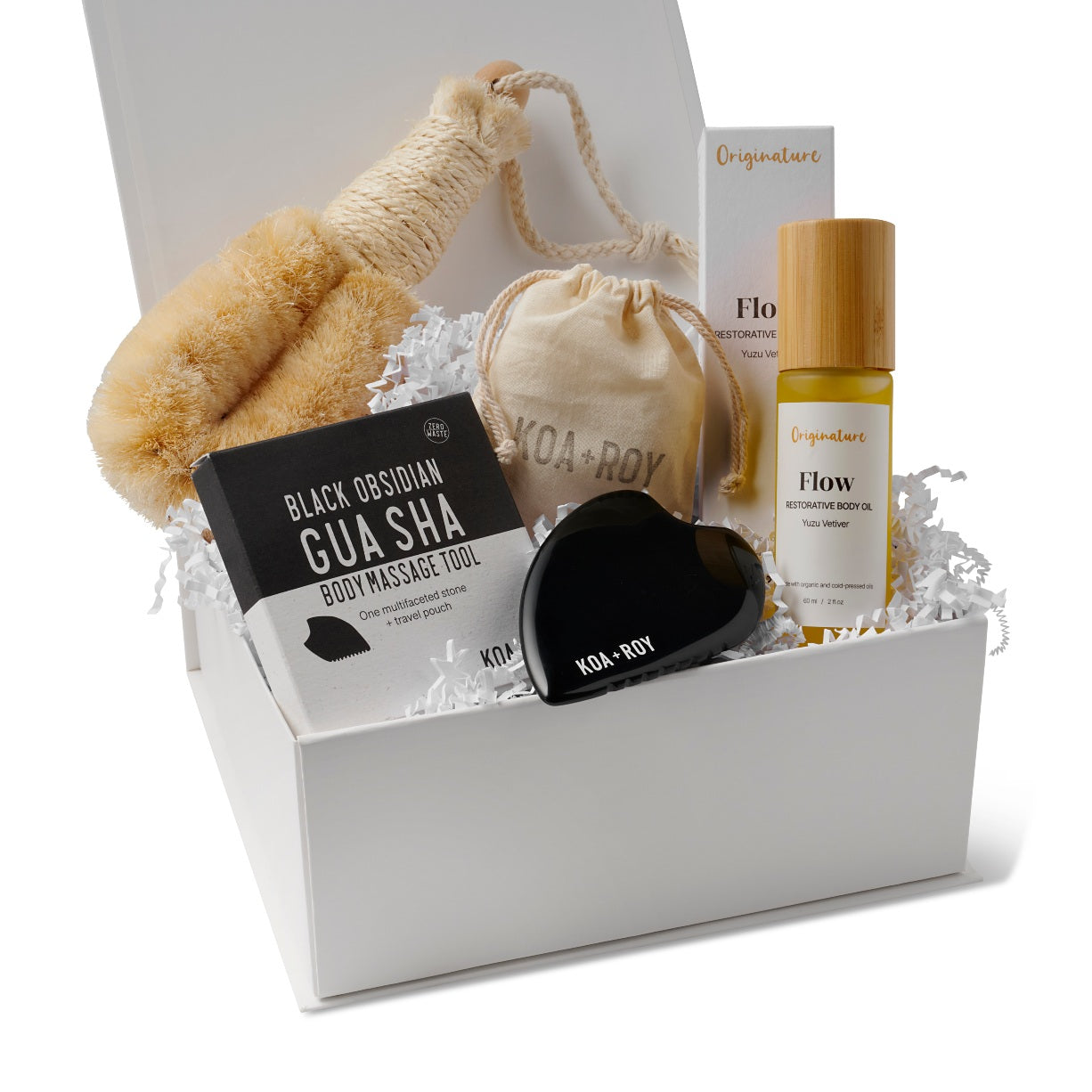Collection of skincare and wellness products including a gua sha tool, body brush, and oil inside the Here I Am Gift box with white crinkle paper filling. 