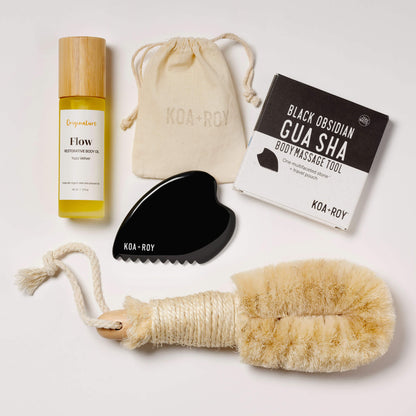 Self-care products including body oil, dry brush, and gua sha tool on a white background