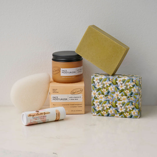 Skincare products in the Fresh Face box on a counter, including lip balm, a face moisturizer, soap made with sandalwood essential oil, and a konjac sponge.