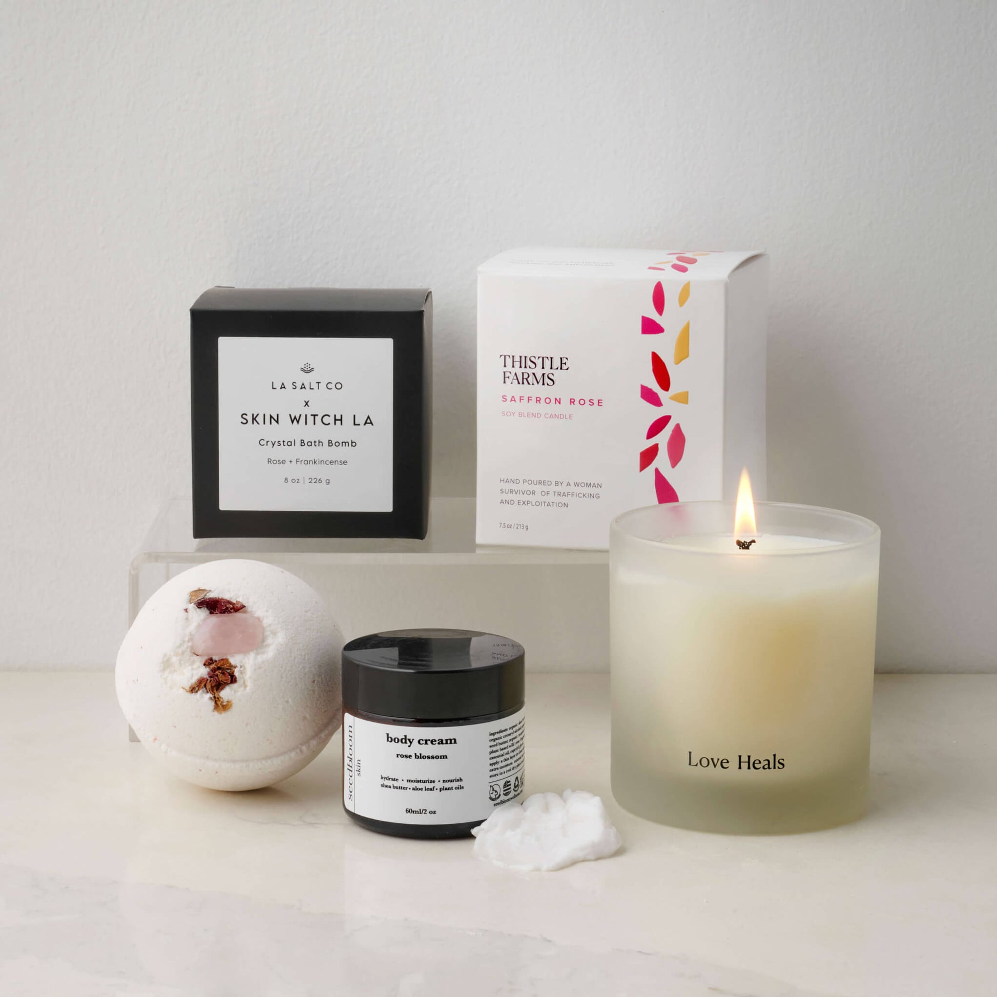 Love Heals candle with rose blossom lotion and a rose crystal bath bomb on a counter