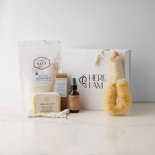 Contents in the Magnesium Bath Box, including Zechstein sea salts, body brush, shower spray, and soap with a Here I Am giftbox in the background.