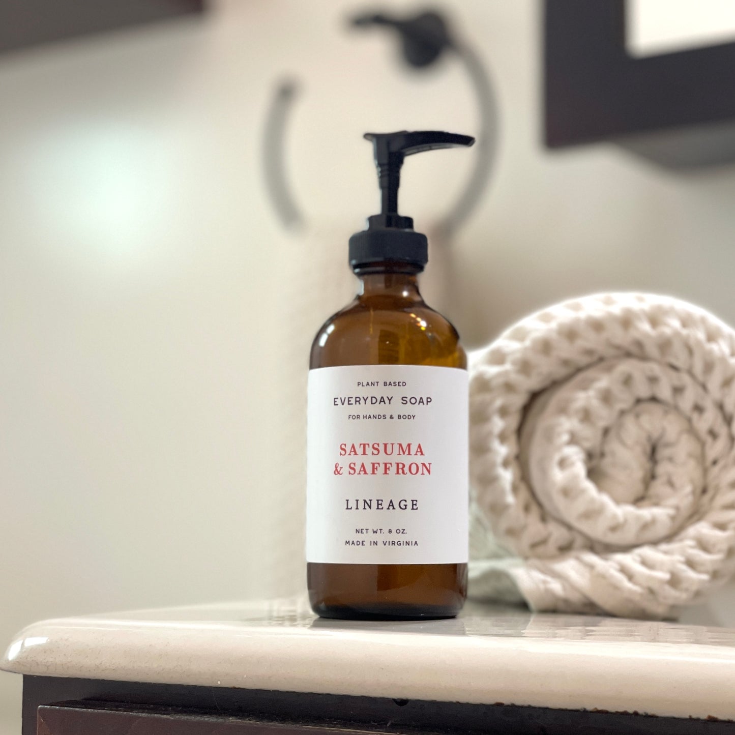 Bottle of Satsuma & Saffron liquid soap on bathroom counter with towel