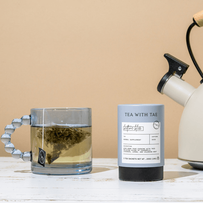 Bedtime Bliss herbal tea from Tea with Tae next to a glass mug with tea on a wooden surface.