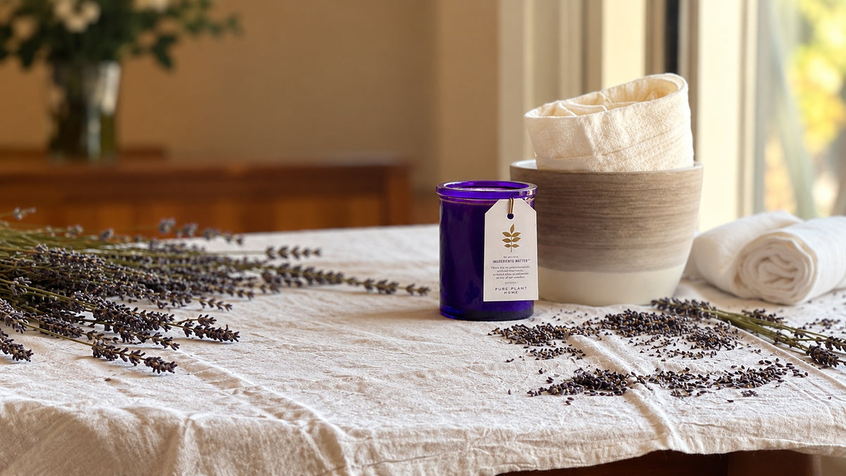 Fresh lavender and an essential oil candle are displayed as part of a self-care routine with flowers and towels by a sunny window.