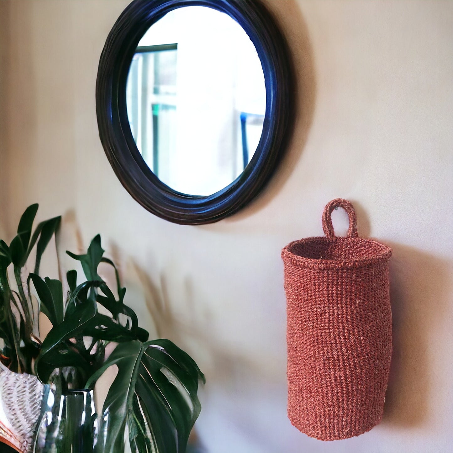 Woven storage basket on wall next to round mirror and greenery
