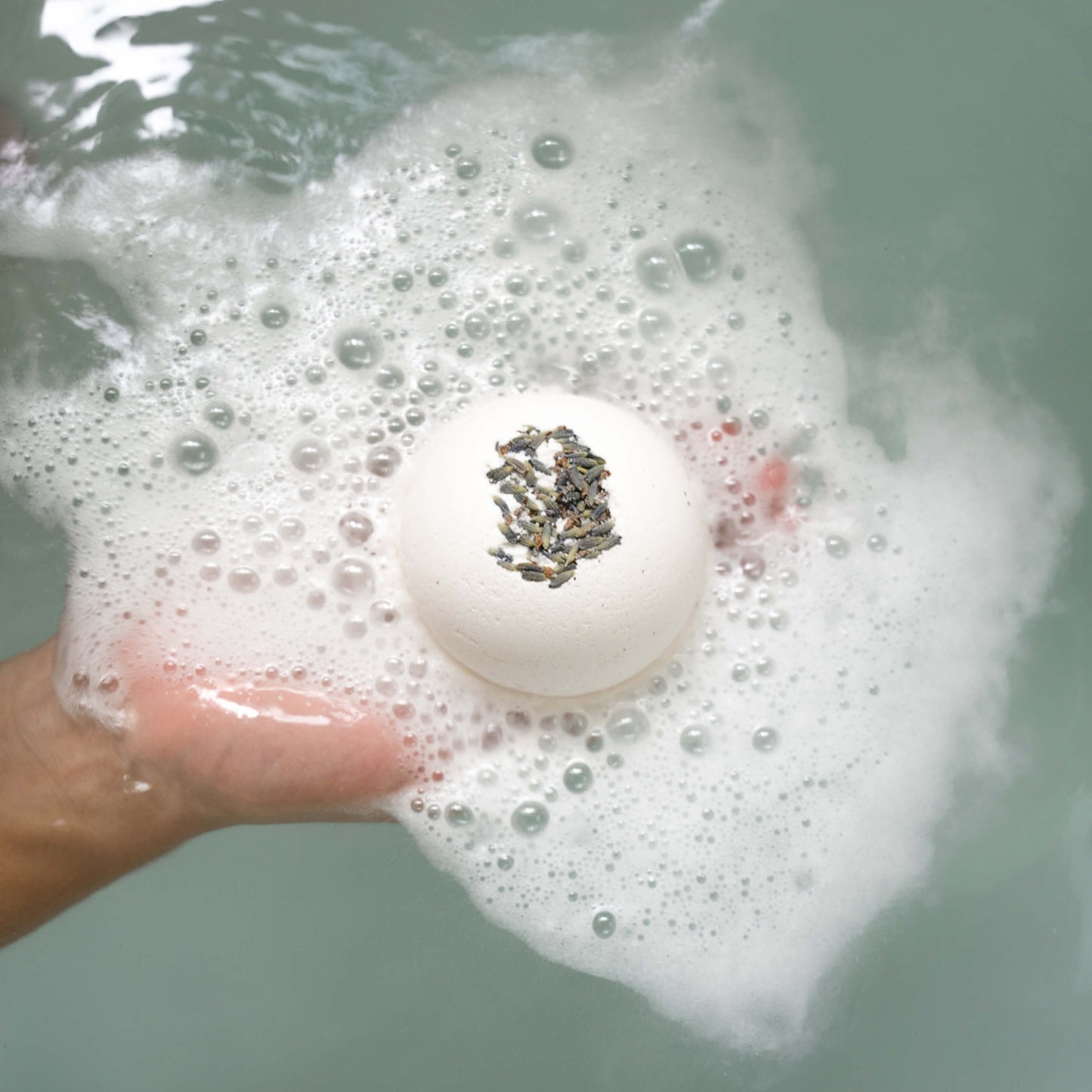 Hands holding the Zen bath bomb as it foams in a tub  of water