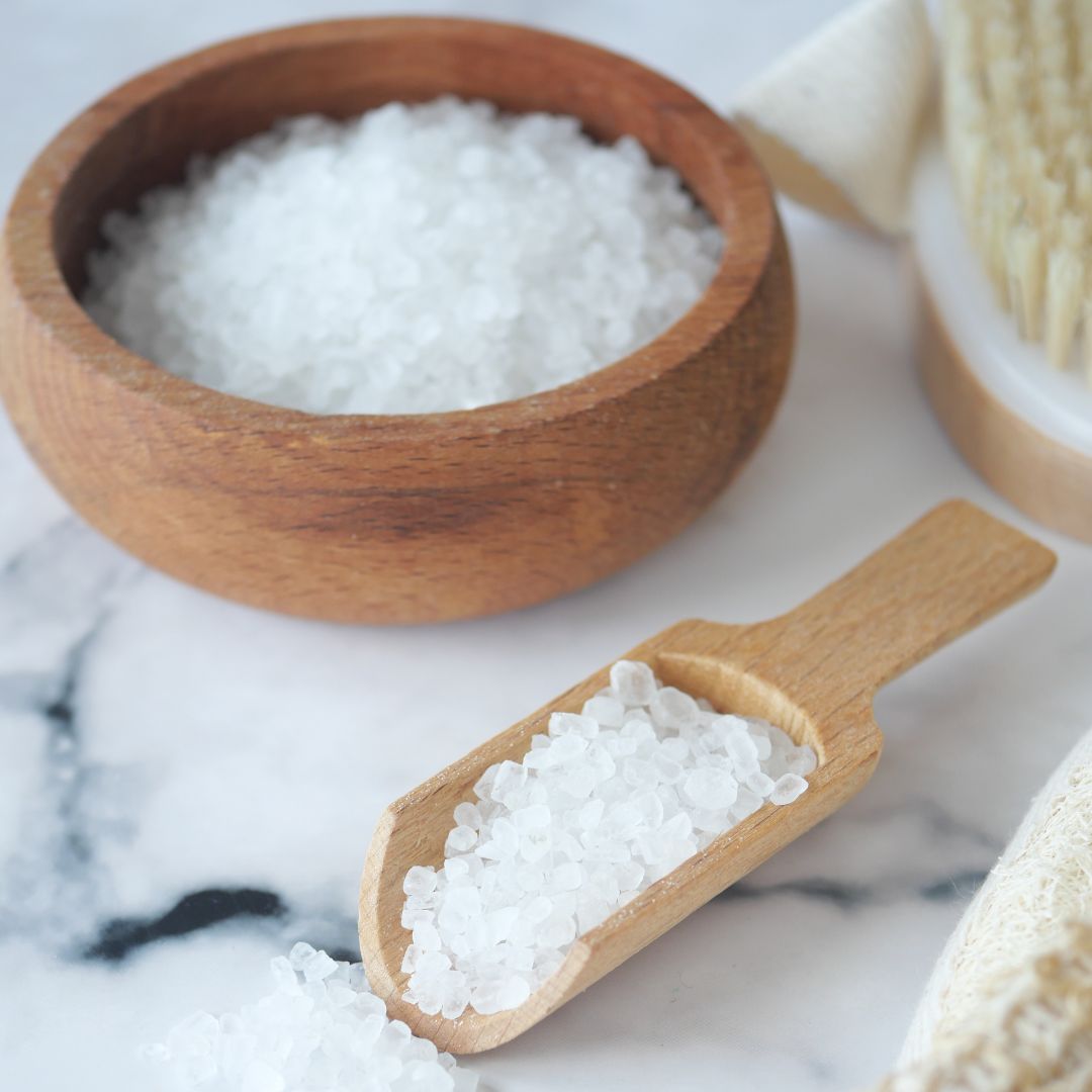 Wooden bowl and scoop filled with magnesium foot soak on a marble surface