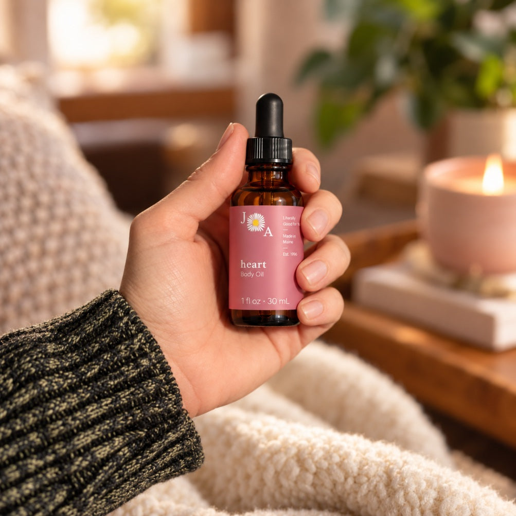 Woman holding an amber glass dropper bottle labeled with the Heart Floral Aromatherapy body oil in a warm indoor setting.