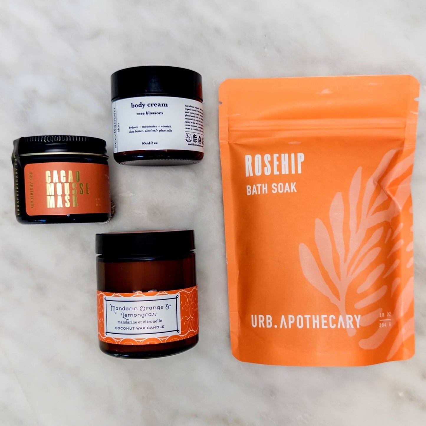 Collection of self-care products in the Blissful Bath set with the Cacao mask, mandarin orange lemongrass candle, floral hand lotion and rosehip bath soak.