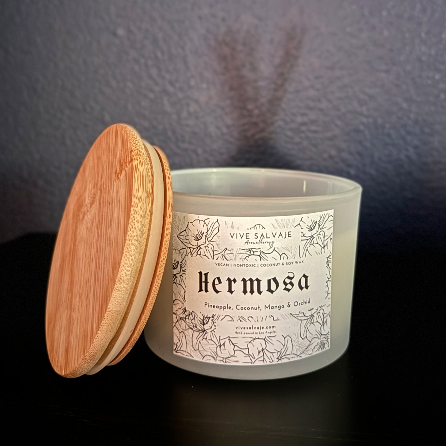 The Hermosa Three Wick candle on a table with blue background