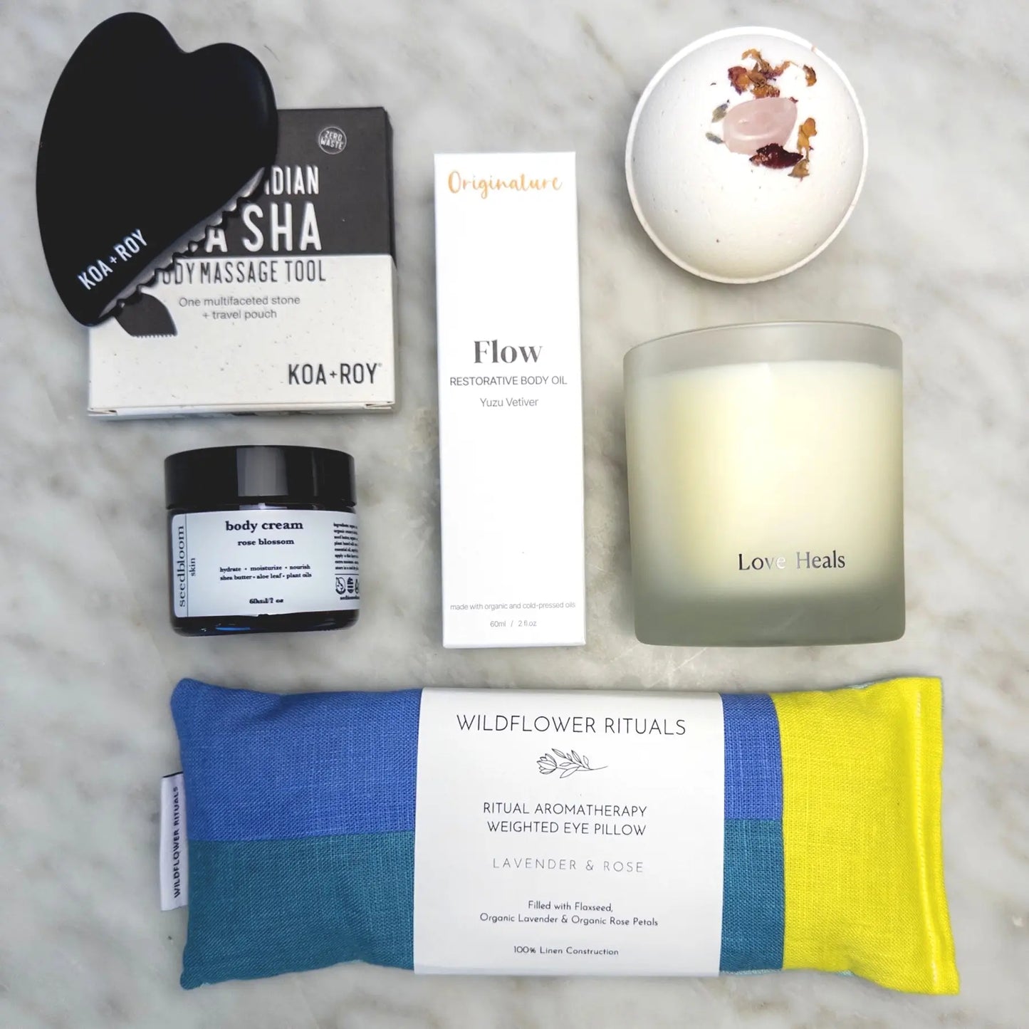 Collection of wellness products from the Luxury Spa Gift Box, including a weighted eye pillow, candle, and skincare items on a marble surface.