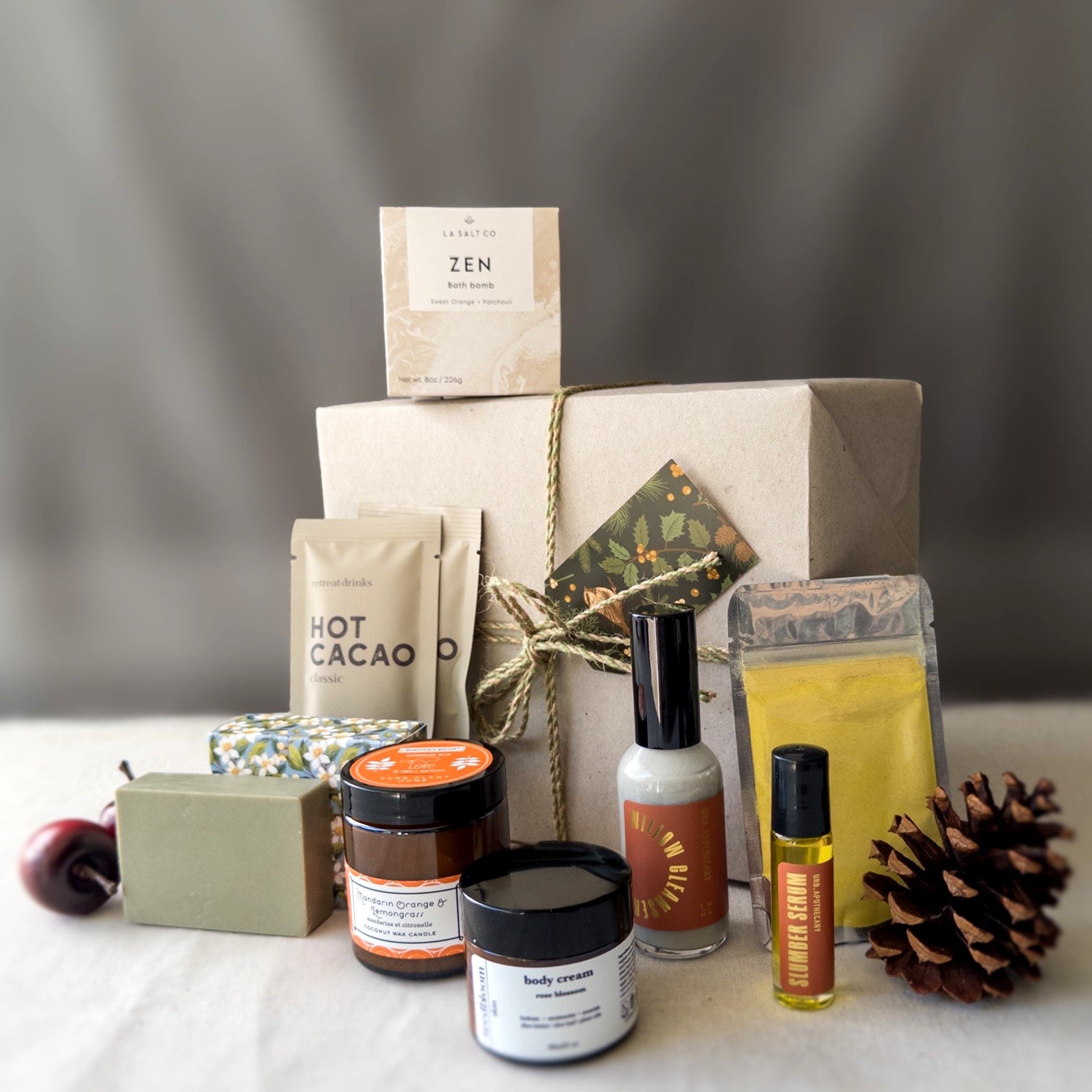 Collection of wellness products in the New Mom Self-Care Gift Box, including hot cacao, a turmeric face mask, and various other skincare products in front of a wrapped gift box. 