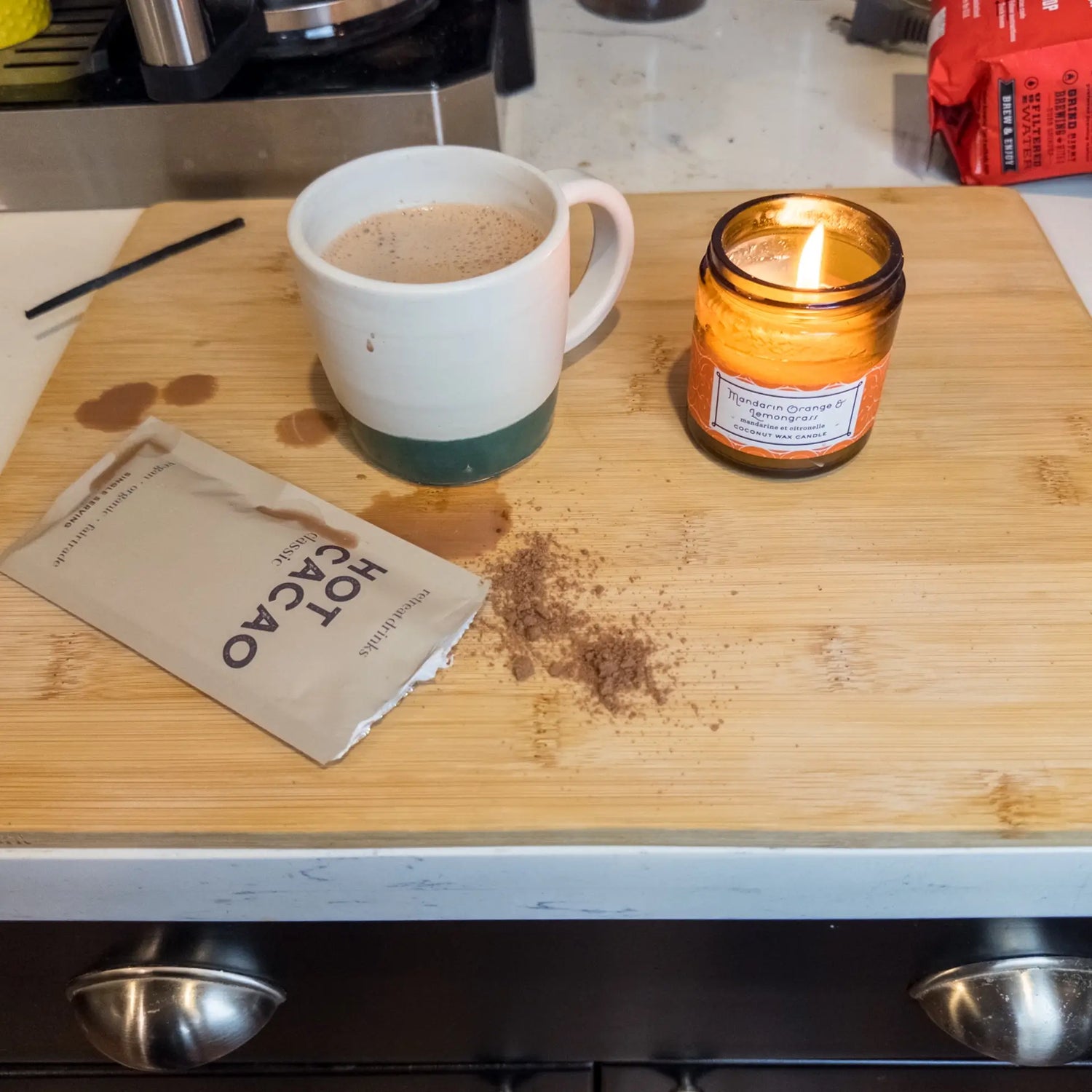 The New Mom gift box with a mug of hot cacao and the mandarin orange lemongrass candle on a counter.