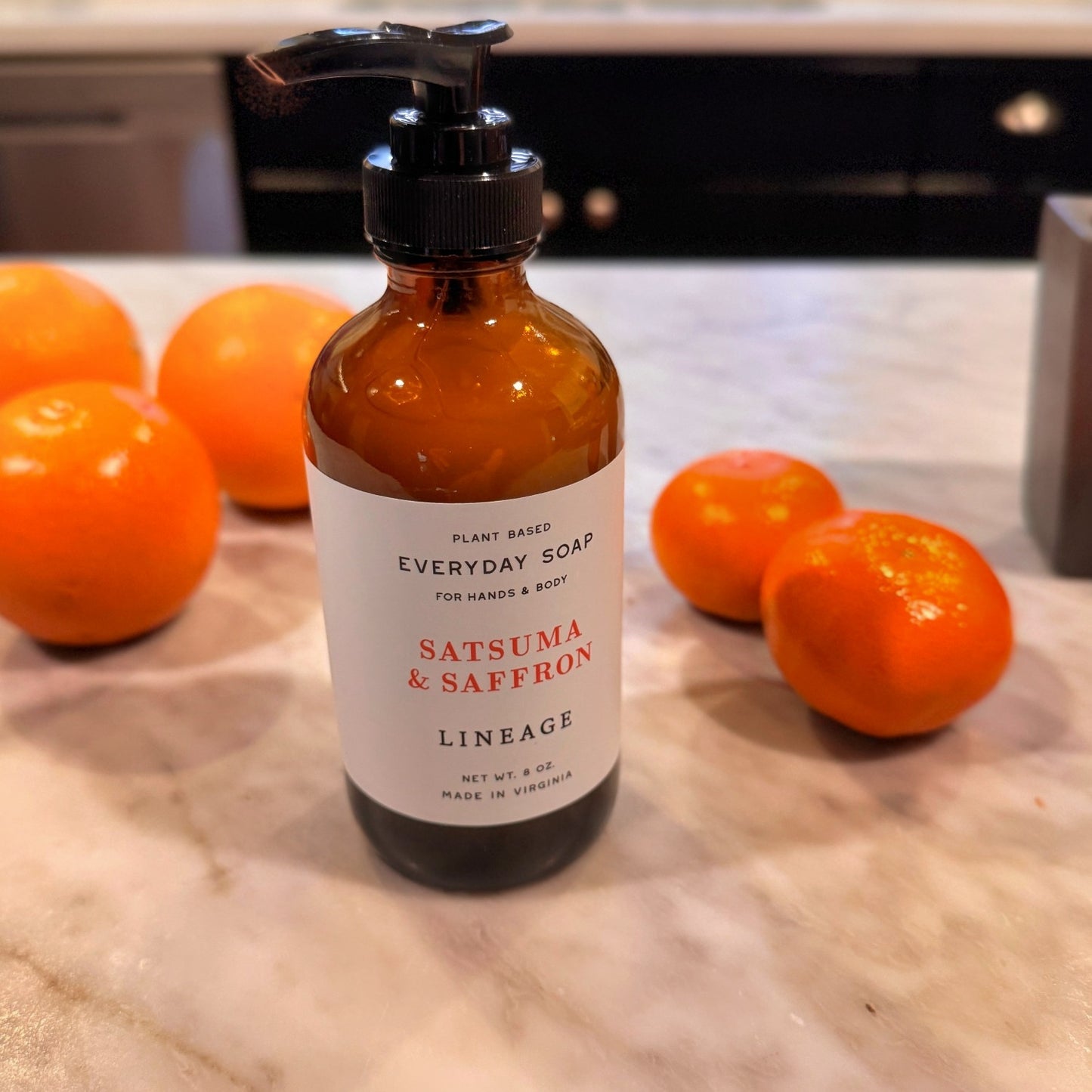 Bottle of Satsuma & Saffron liquid soap on counter with oranges and tangerines