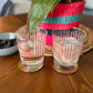 Set of two old fashioned glasses with retro pink and orange design in front of the pink basket