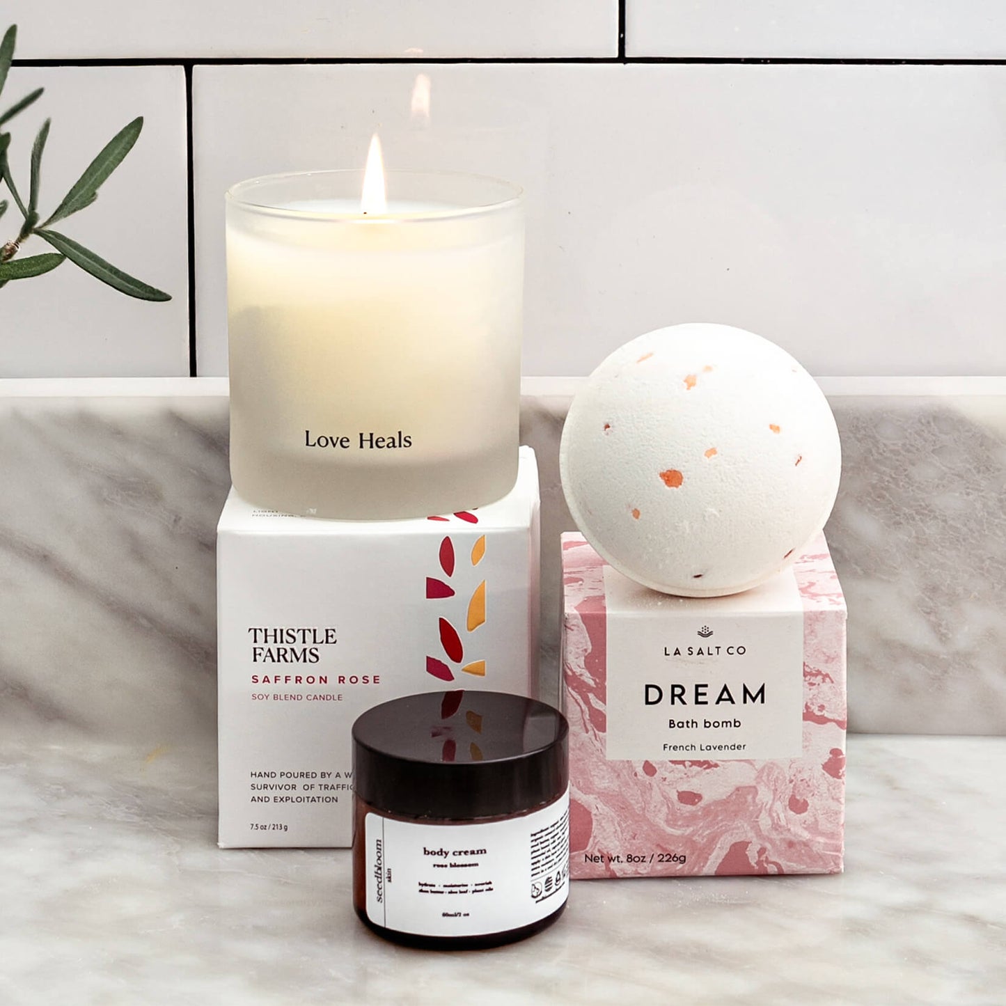 A Valentine gift that gives back, with candle, bath bomb, and body cream on a marble surface with a white tiled background.