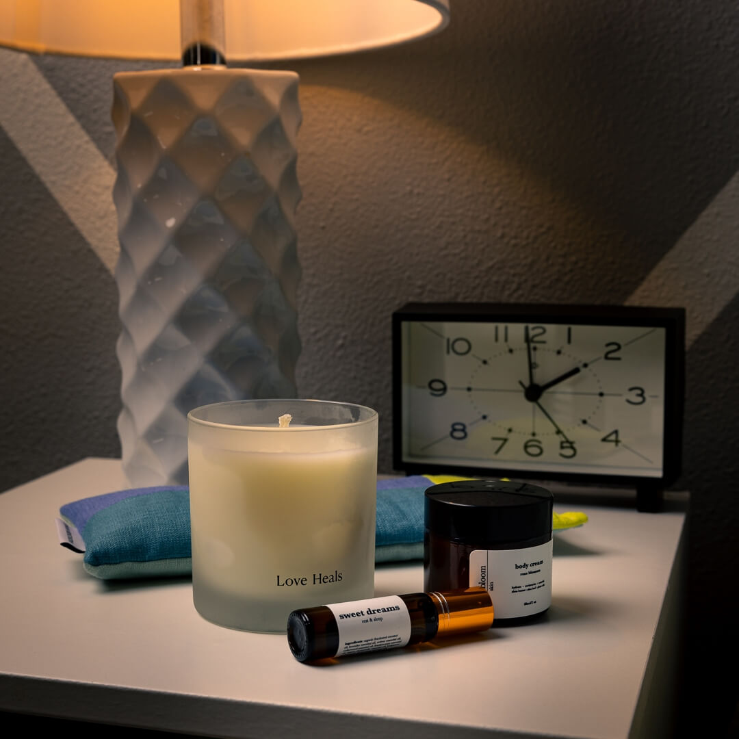 Candle, aromatherapy, lotion, and eye pillow on a nightstand with lamp and clock