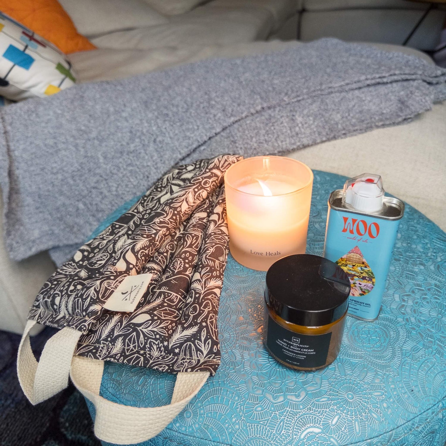 The Rest & Relaxation Box with neck wrap, candle, blue tansy oil, and lavender lotion by a cozy couch. 