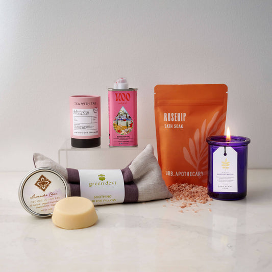 Collection of wellness products with Rosehips and Lavender including a candle, bath salt, and towel on a white surface with a branded box in the background.