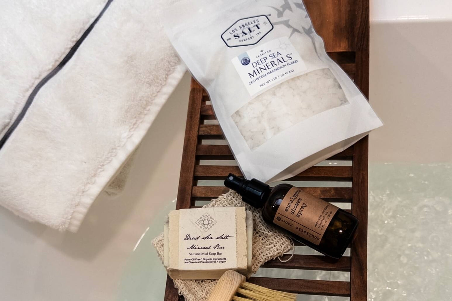 The Mineral Rescue box with magnesium salts, eucalyptus spray, and exfoliators over a bathtub. 
