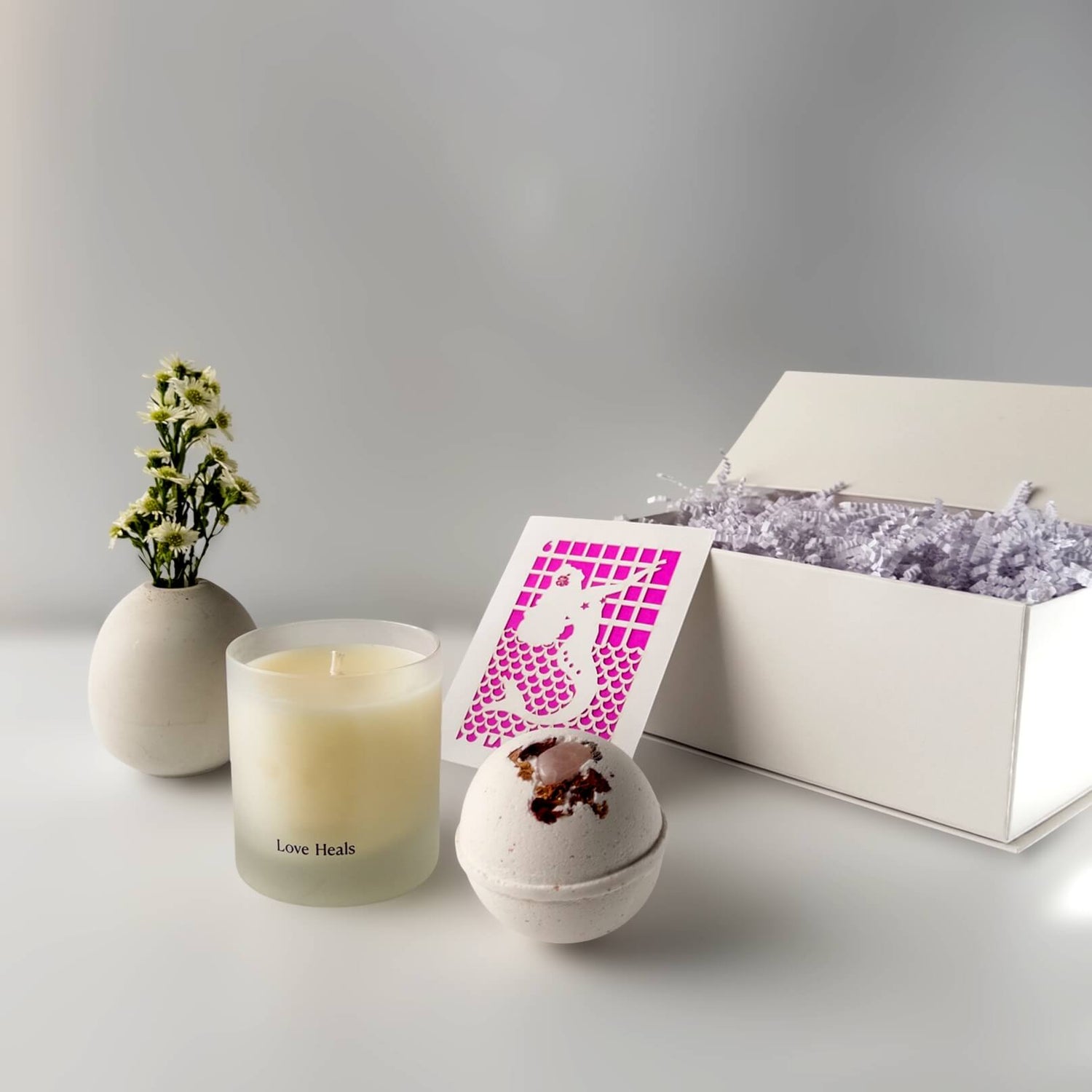 Candle, bath bomb, and gift box on a white surface with a gray background