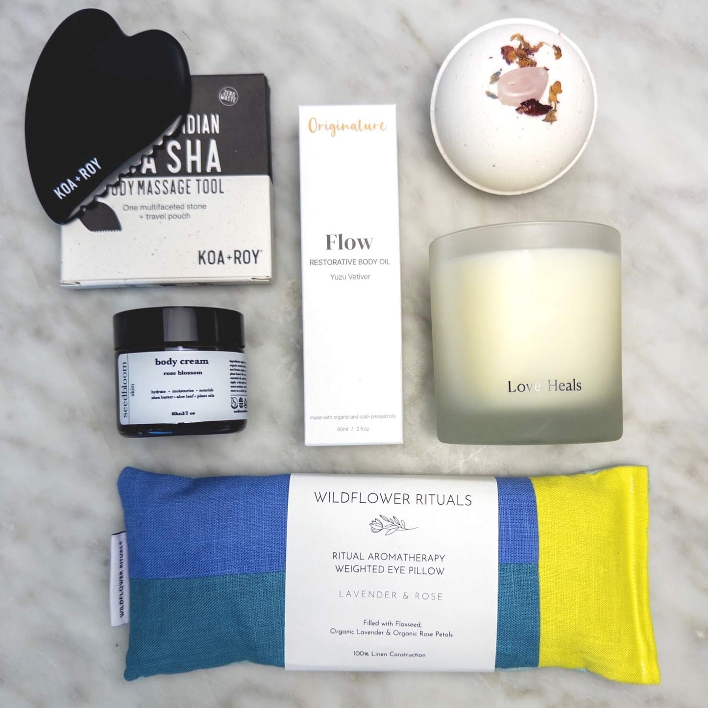 Collection of wellness products from the Luxury Spa Gift Box, including a weighted eye pillow, candle, and skincare items on a marble surface.