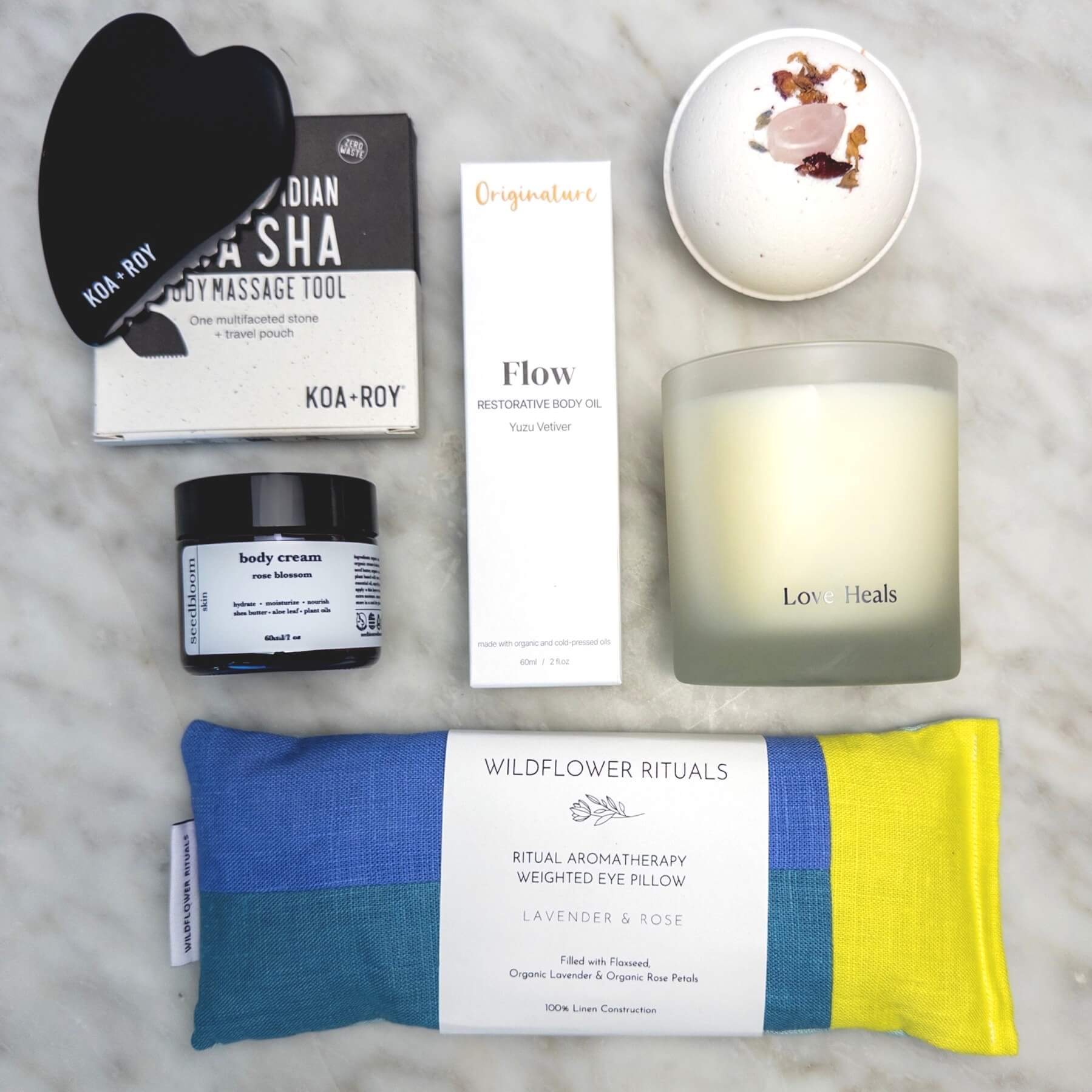 Collection of wellness products from the Luxury Spa Gift Box, including a weighted eye pillow, candle, and skincare items on a marble surface.
