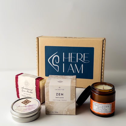 Collection of wellness products from the Zen Moment box, including candles and bath salts with 'HERE I AM' branded box on a white background.