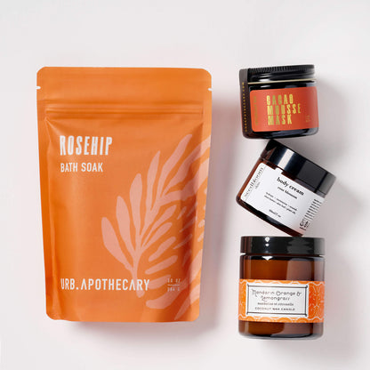 Collection of self-care products in the Bliss box set with the Cacao mask, mandarin orange lemongrass candle, floral hand lotion and rosehip bath soak.