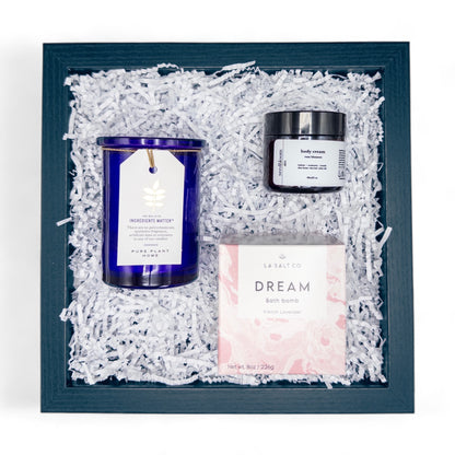 Lavender Dreams Bath Box, a curated collection of a bath bomb, aromatherapy candle, and rosehip moisturizer in a box on white crinkle paper