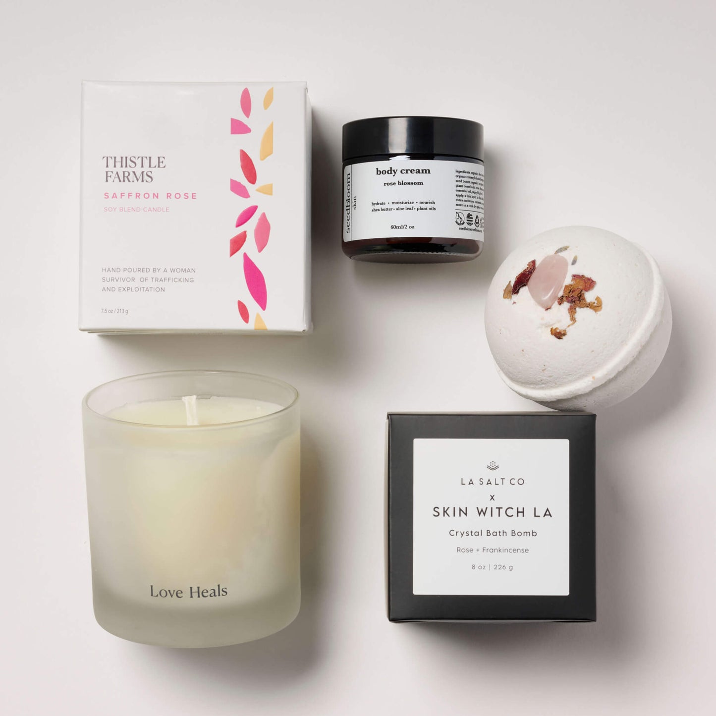 Love Heals candle with rose blossom lotion and a rose crystal bath bomb on a white tile background