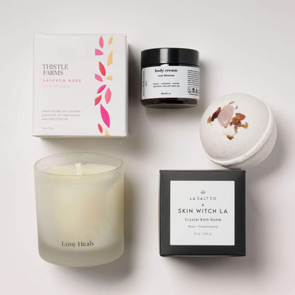 Love Heals candle with rose blossom lotion and a rose crystal bath bomb on a white tile background